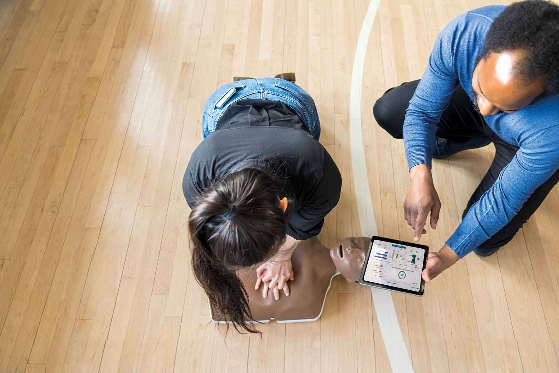 bystanders performing cpr on little anne qcpr on a basketball court
