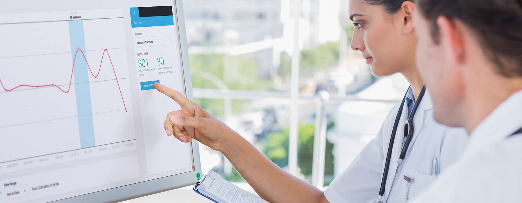 Two people working together on a large computer screen. A woman is pointing  at the screen.