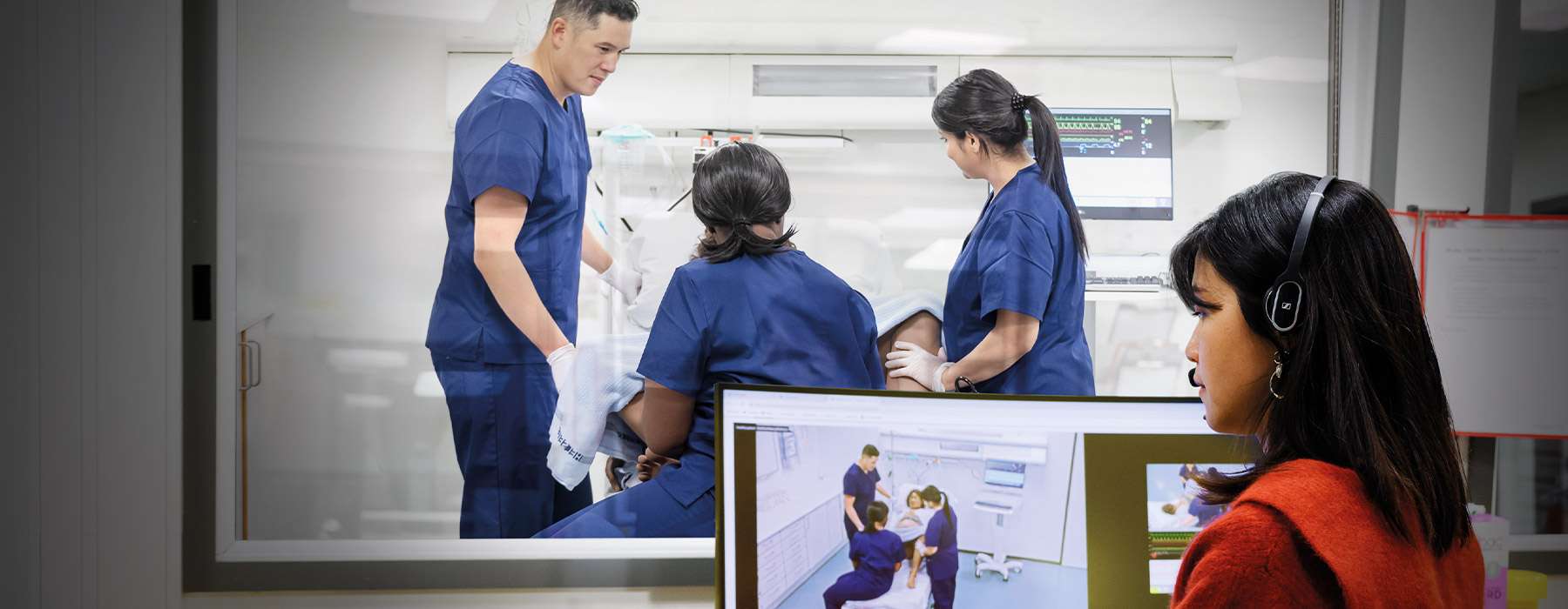 Three nurses working on a simulation in a room, while a woman follows their progress onscreen from the control room