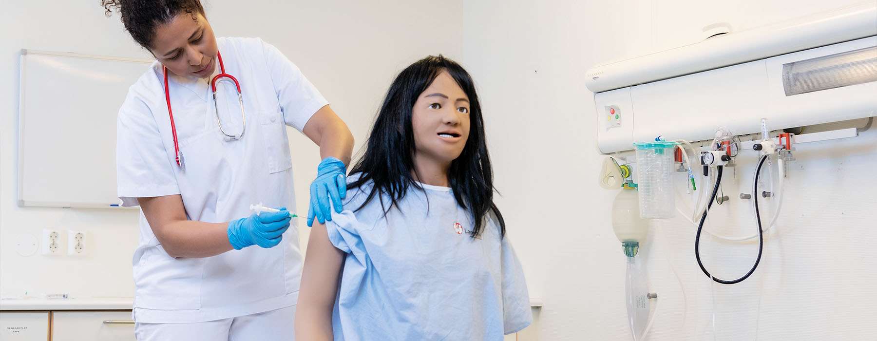 A healthcare student in a clinical lab practicing intramuscular injection techniques on a high-fidelity patient simulator.