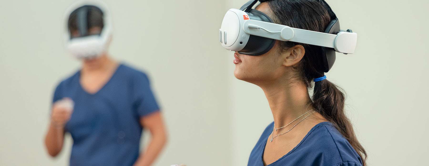Two nursing students wearing VR headsets and using hand controllers to practice clinical scenarios in a virtual environment.