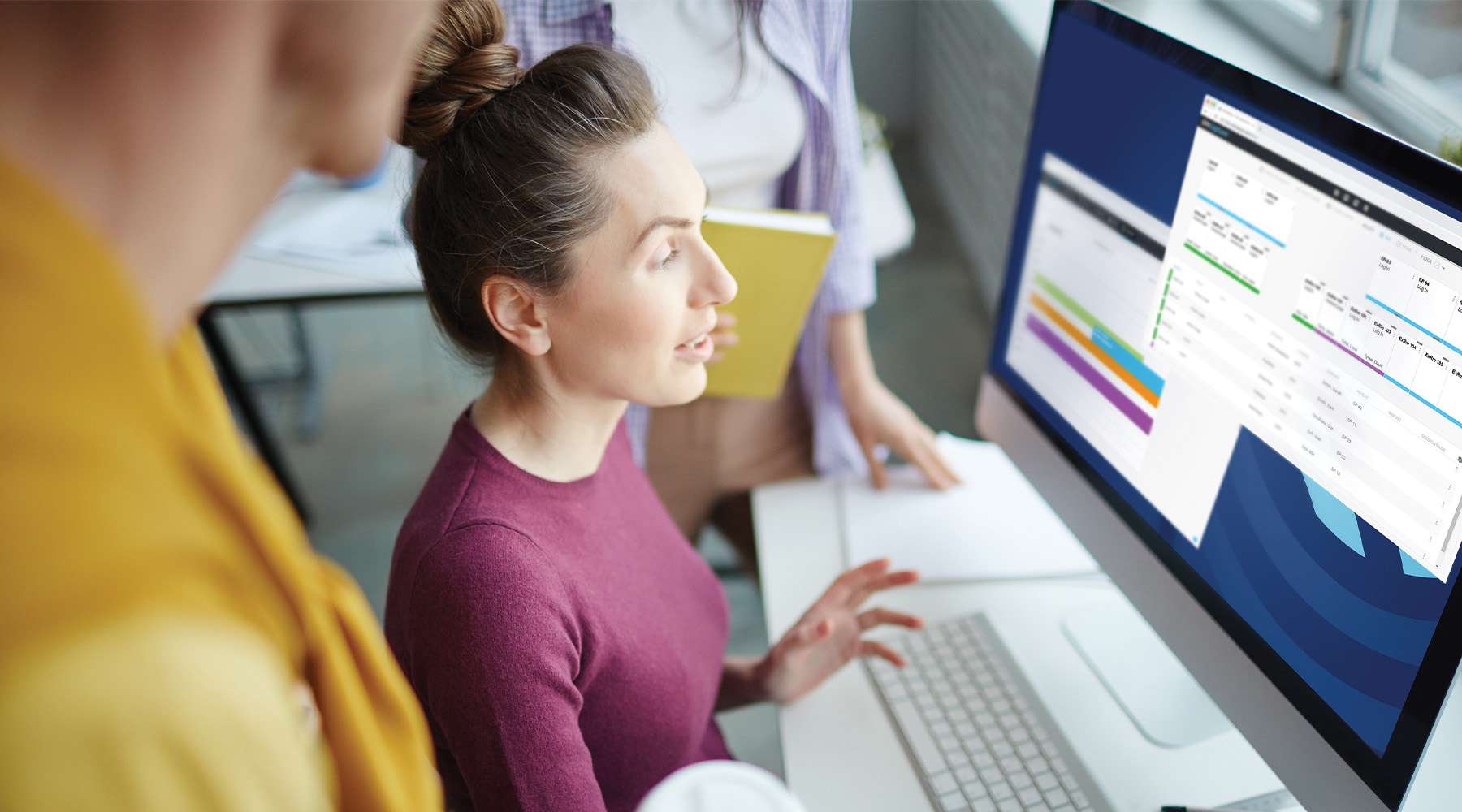 Young creative web-designer or programmer looking at information on display and discussing it with colleagues