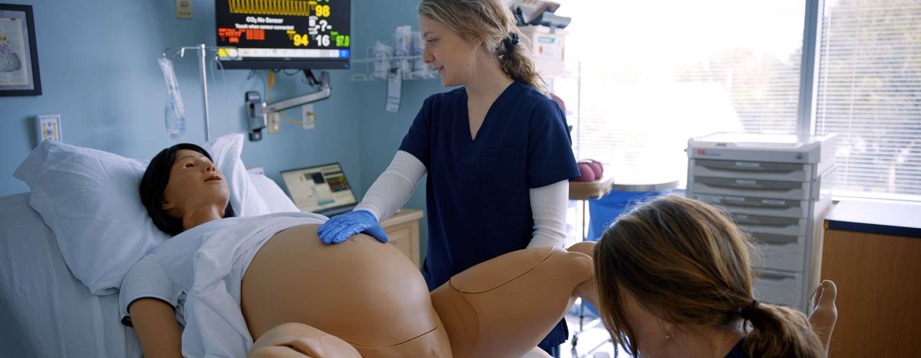 Two healthcare providers managing an active labor scenario using the MamaAnne birthing simulator and electronic fetal monitoring.