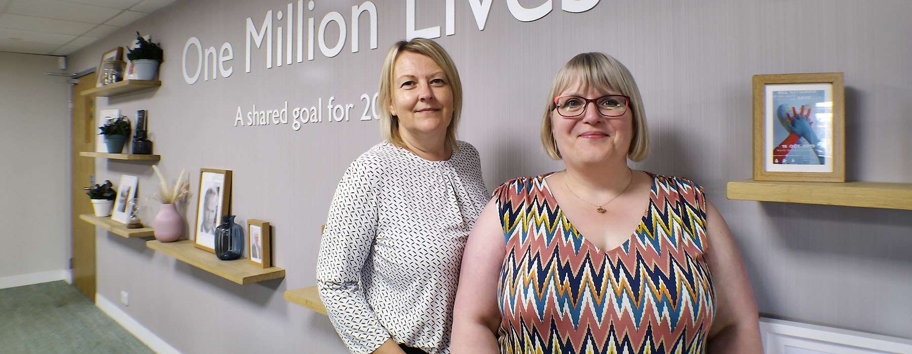 Two women standing in front of Laerdal's "One Million Lives" text on a wall
