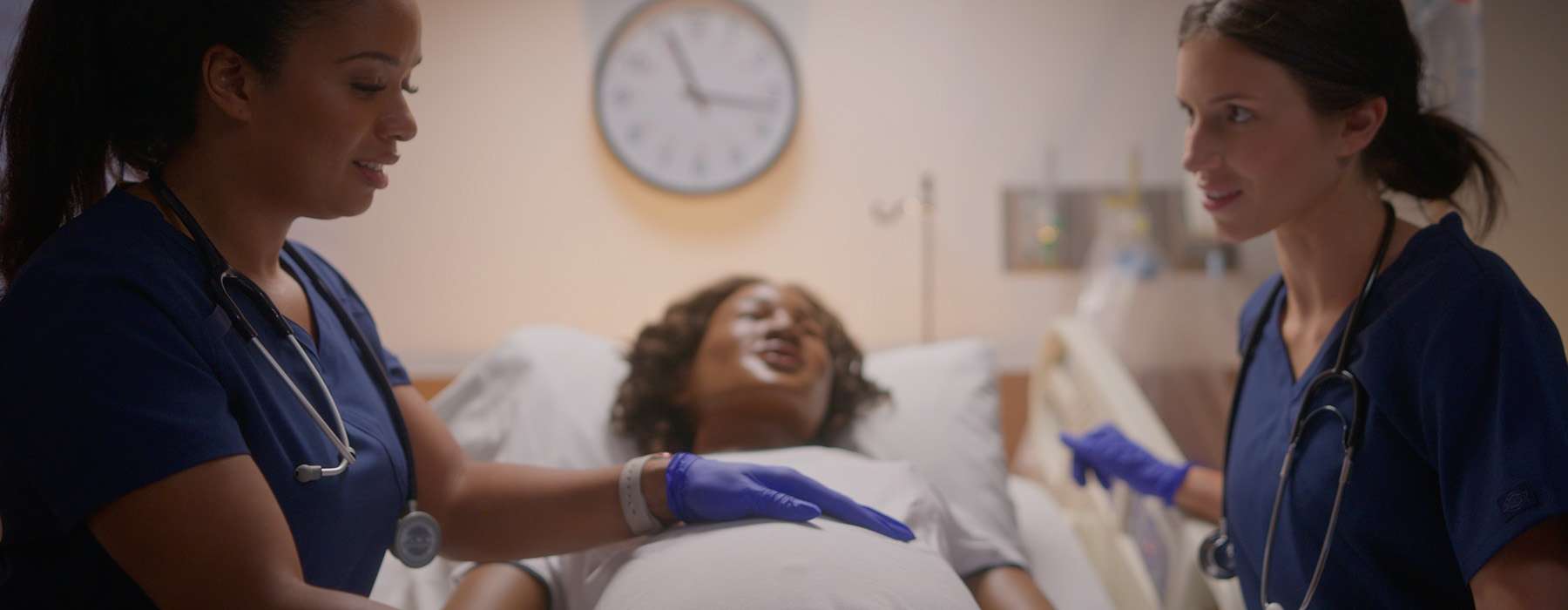 Two nurses on either side of a MamaAnne simulator on a hospital bed.