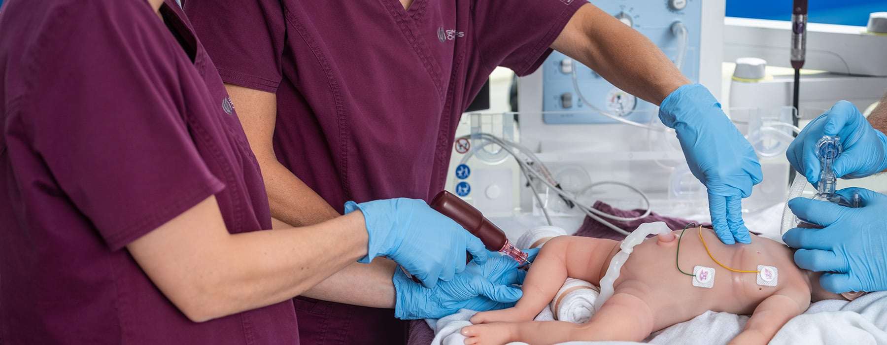 Closeup of the arms and glowed hands of three healthcare professionals using a baby manikin for simulation training.