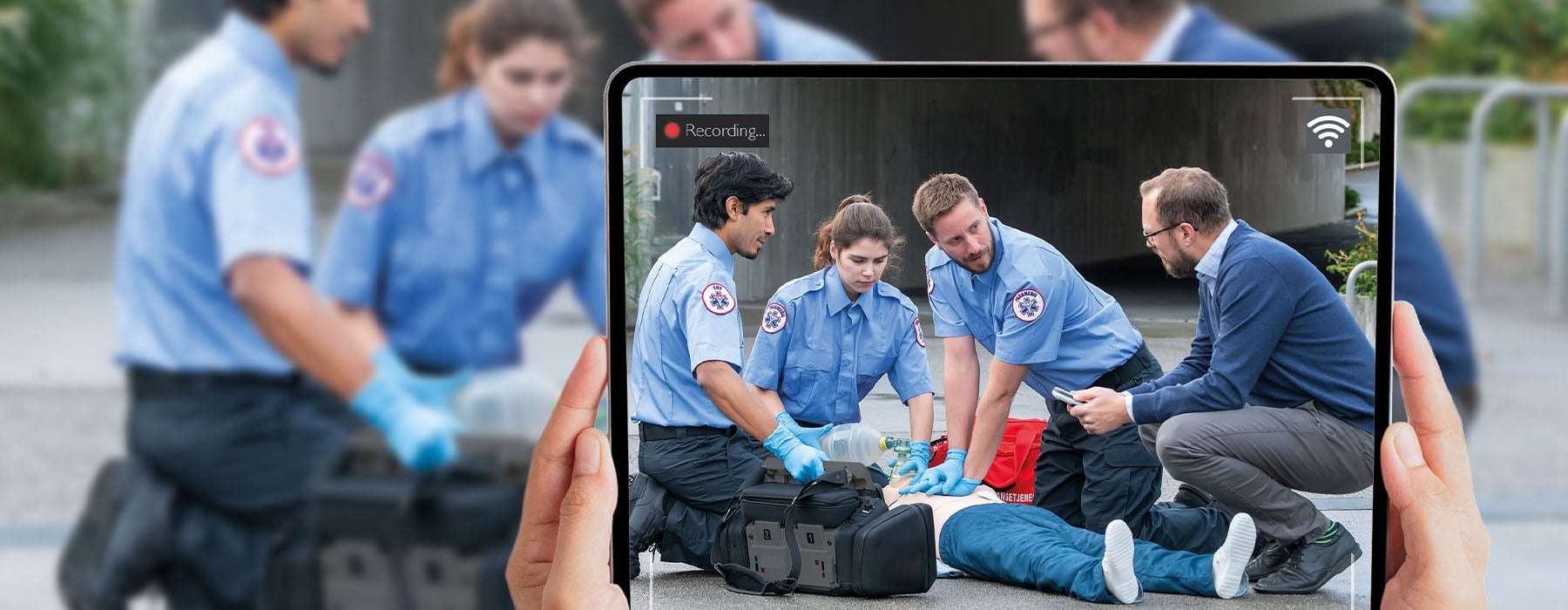Hands holding up a tablet while recording EMS training happening outside, in a natural environment