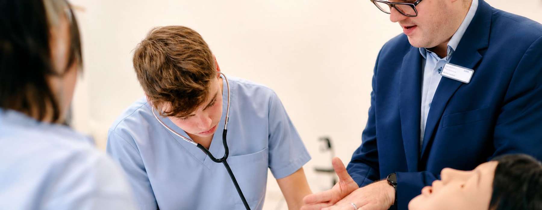 Training situation. Student using stethoscope on manikin while being guided by an instructor.