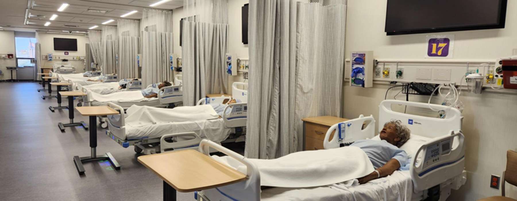 A row of hospital beds, each containing a training manikin.