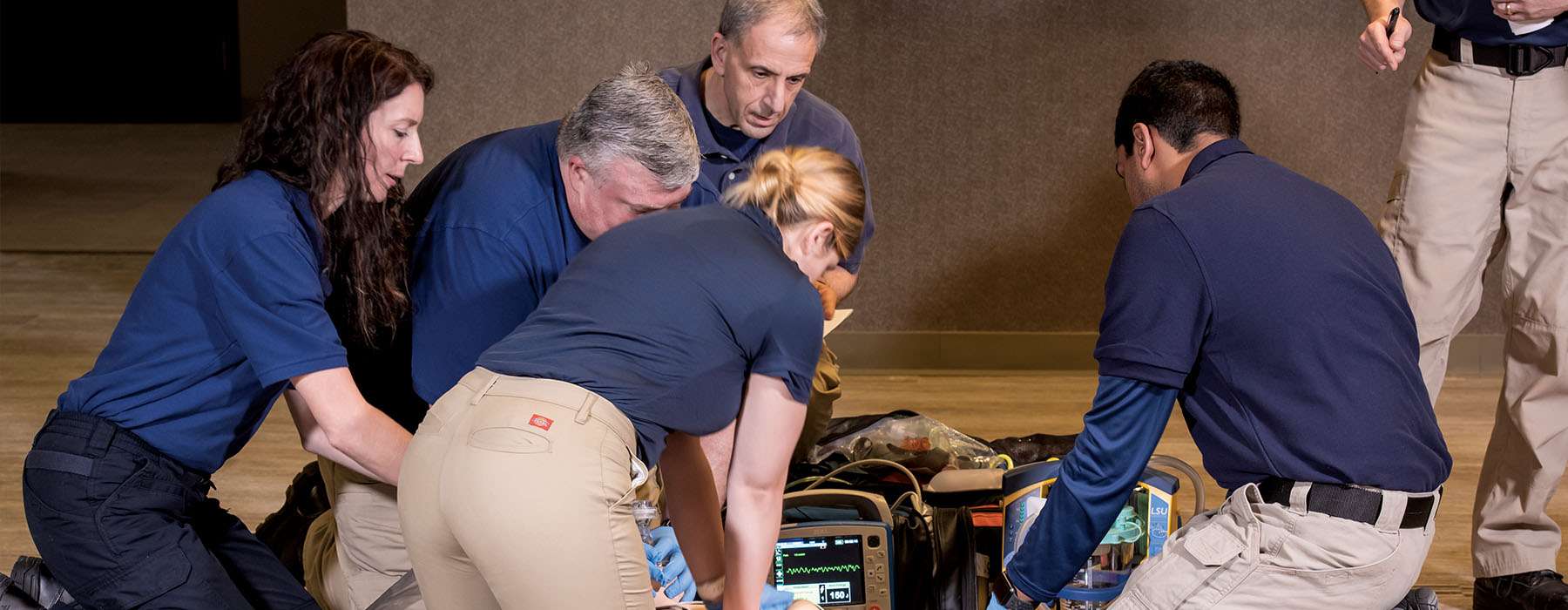 Group of five people wearing blue shirts performing CPR training.