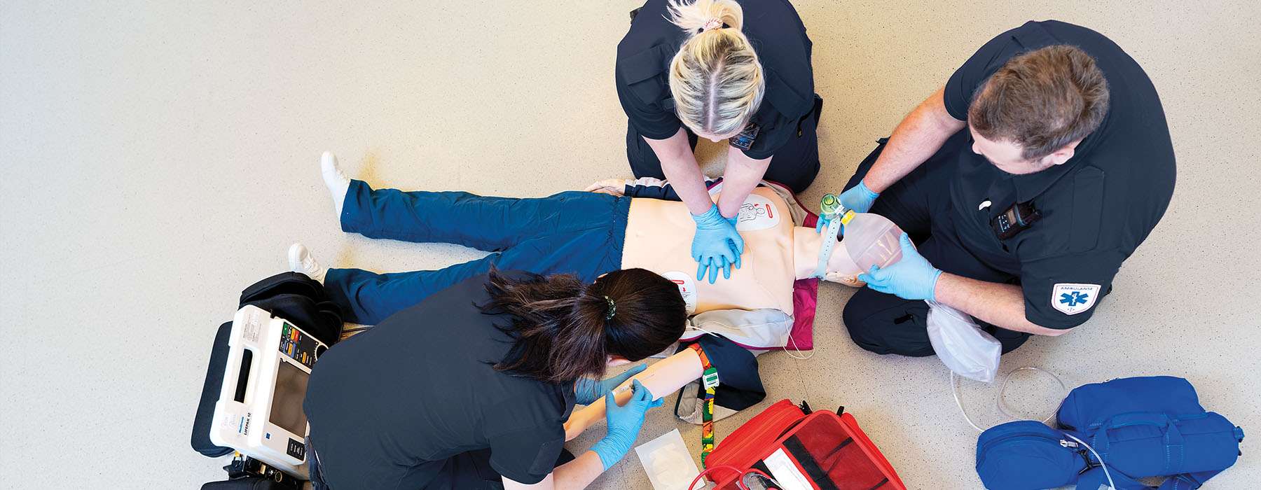 View from above: Three people doing CPR training on a manikin.