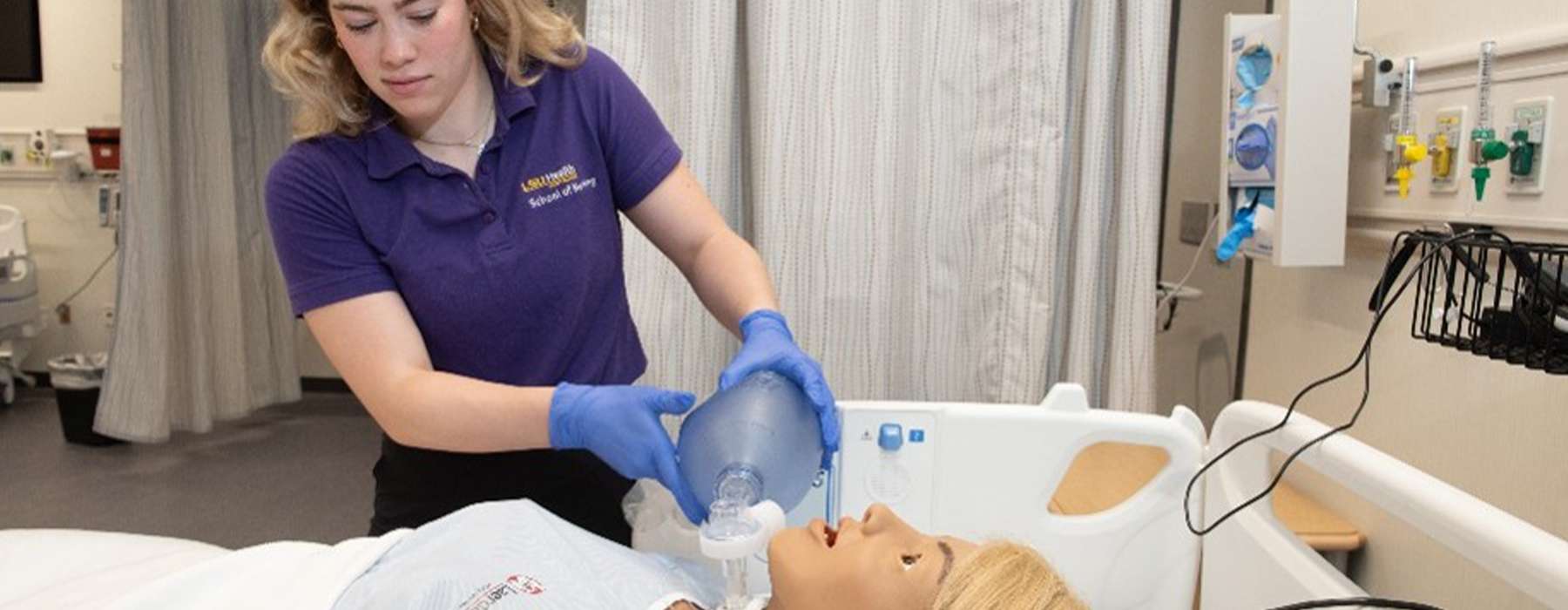 A nursing student wearing a purple shirt training using a manikin.
