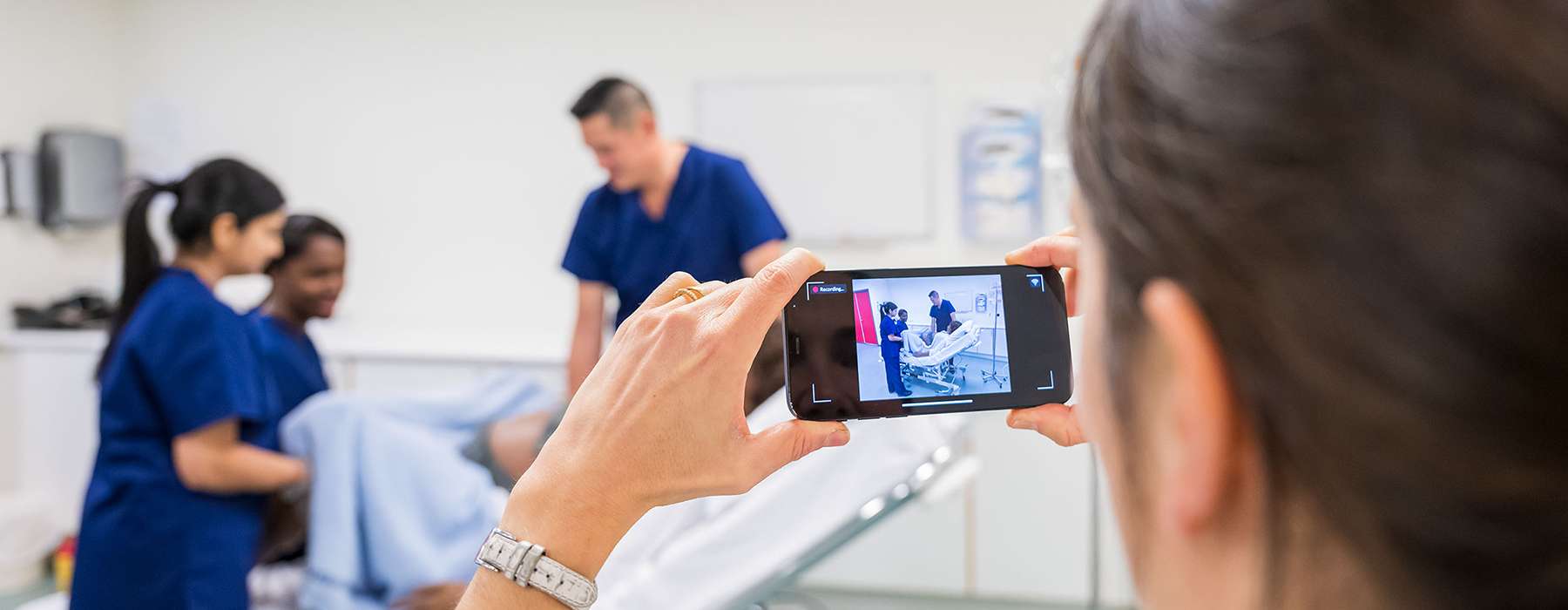 woman holding a phone with camera turned towards three nurses working, using SimCapture