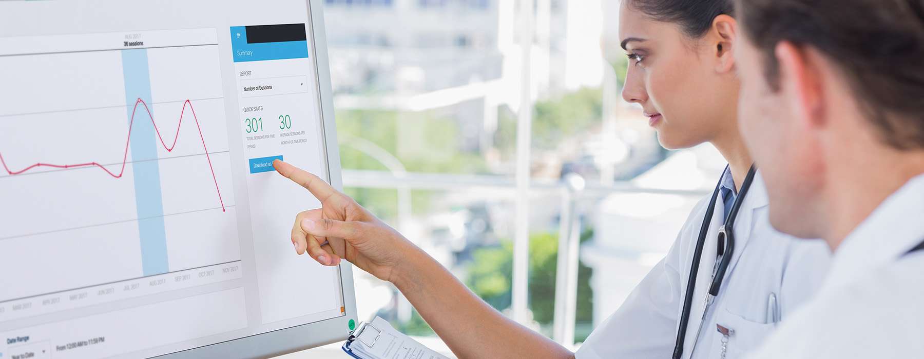 Two healthcare professionals reviewing clinical data and performance trends on a large digital display.